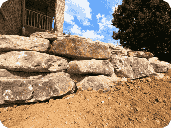 A boulder wall accentuating a residential home surrounded by fresh topsoil