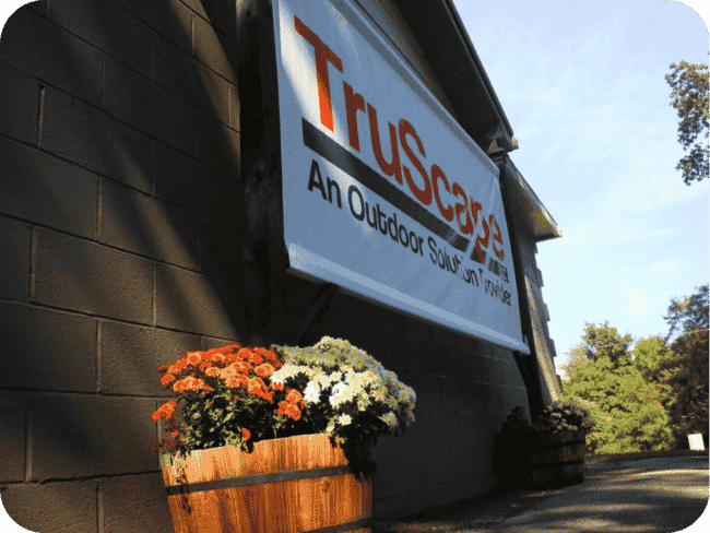 Building with a "TruScape" banner and wooden planters filled with orange and white flowers.