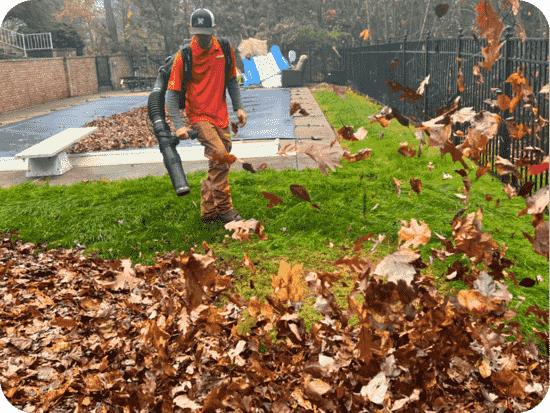 A TruScape Employee dressed in an orange polo shirt blowing fall leaves. 