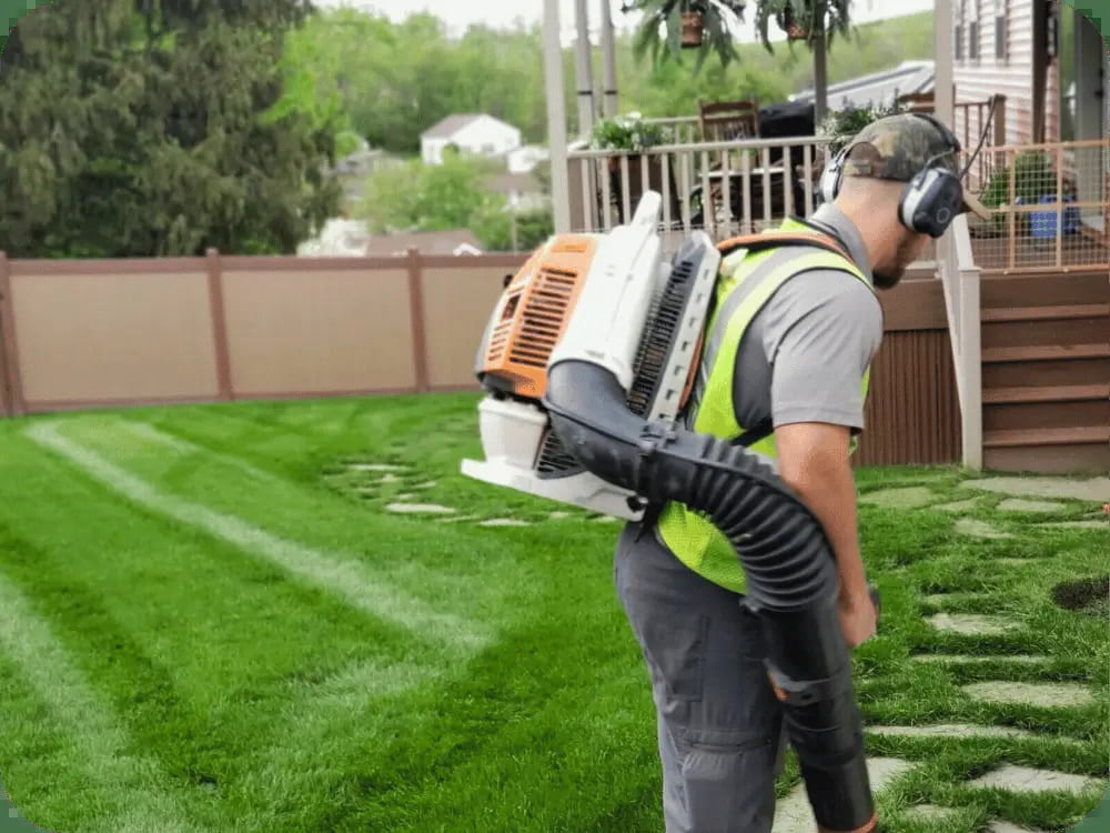 Landscaper using a leaf blower to clean a residential yard with freshly mowed grass.