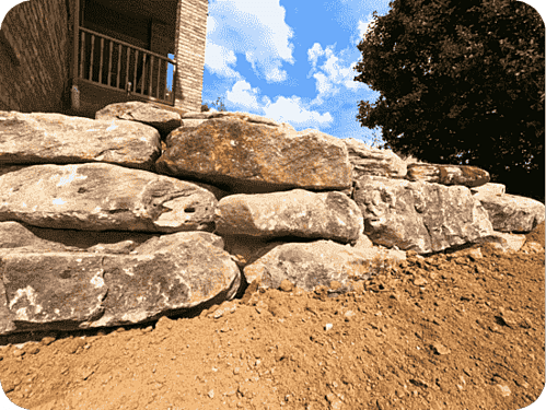 A boulder wall accentuating a residential home surrounded by fresh topsoil