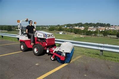 An employee on a tractor sweeping a roadway. 