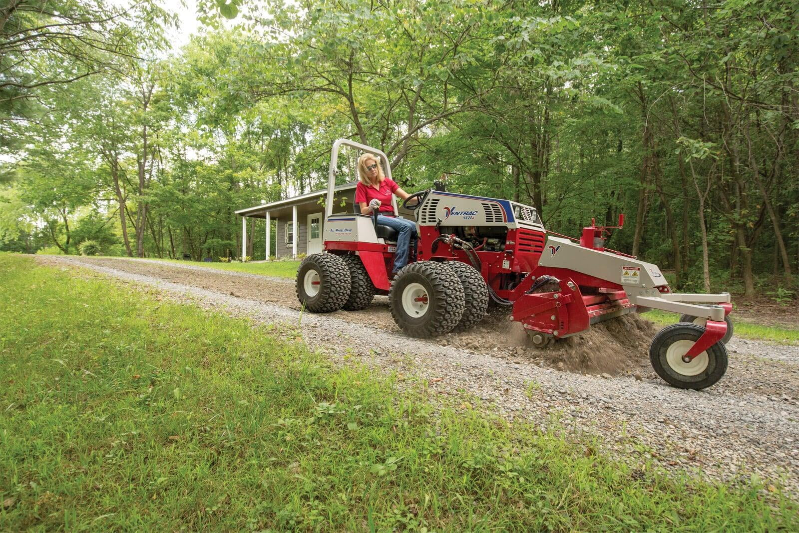 A woman in a red shirt on an articulating tractor grading a gravel driveway with a harley rake. 