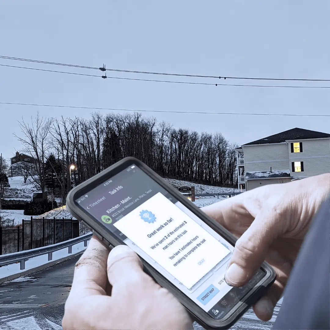 A person using a smartphone outdoors, receiving a job completion notification while standing near a snow-covered road and buildings.