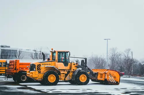 A yellow Volvo front loader parked in a snowy lot, equipped with a large snow pusher attachment.