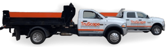 Two TruScape branded white trucks with orange and black accents, one being a dump truck and the other a pickup truck, parked side by side.