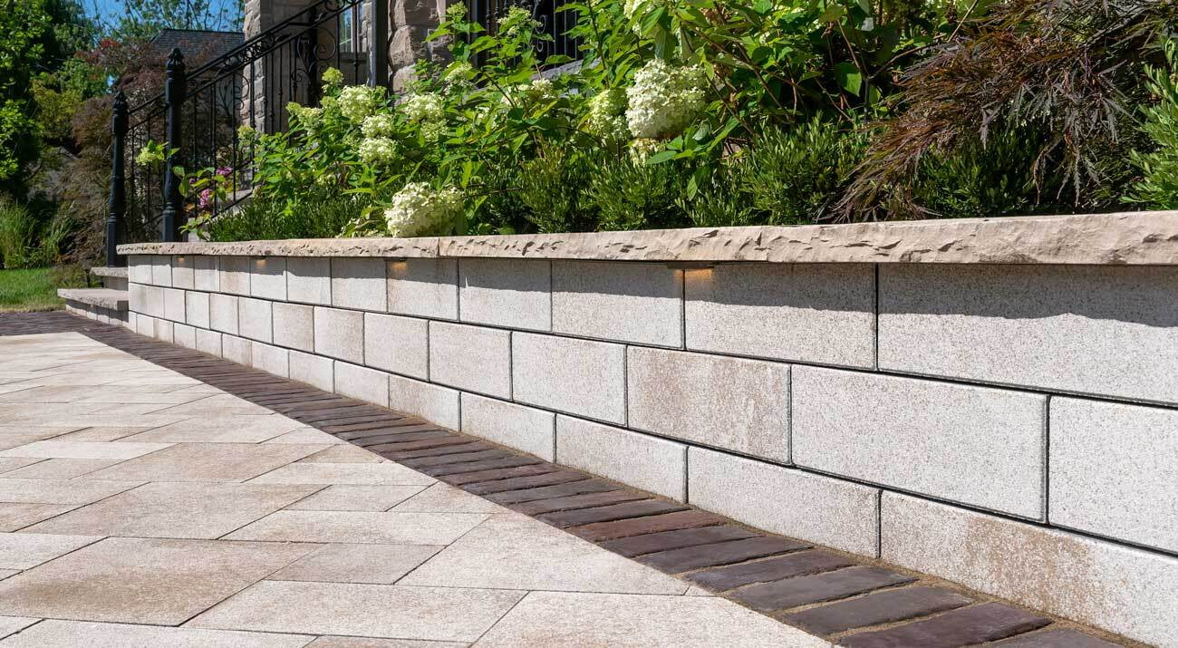 Raised stone flower bed with white hydrangeas and greenery, bordered by a paved patio with brick accents and subtle built-in lighting.